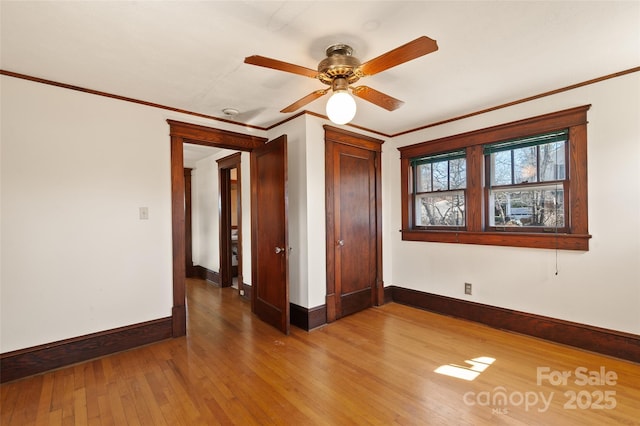 empty room with baseboards, ceiling fan, wood-type flooring, and crown molding