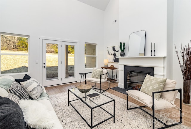 living room with light wood-type flooring, a glass covered fireplace, and high vaulted ceiling