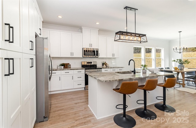 kitchen with appliances with stainless steel finishes, white cabinets, a sink, light stone countertops, and a kitchen breakfast bar