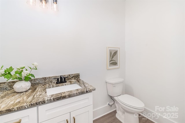 bathroom with wood finished floors, vanity, toilet, and baseboards