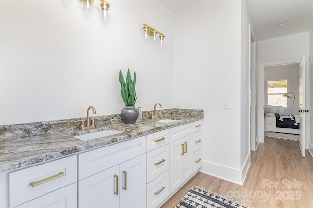 bathroom featuring double vanity, baseboards, a sink, and wood finished floors