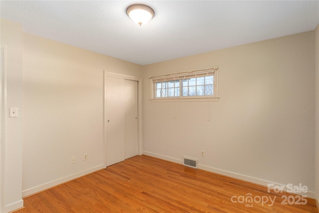 empty room featuring light wood-style flooring, visible vents, and baseboards