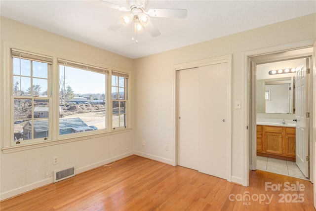 unfurnished bedroom featuring light wood-type flooring, baseboards, visible vents, and a closet