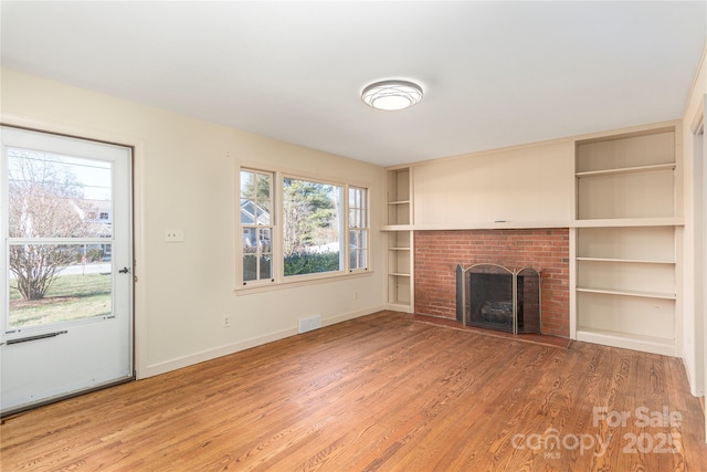 unfurnished living room featuring built in shelves, visible vents, a brick fireplace, light wood-type flooring, and baseboards