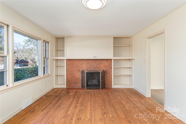 unfurnished living room with built in shelves, visible vents, a fireplace, and wood finished floors