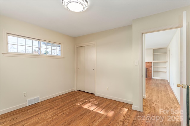 unfurnished bedroom with light wood-style floors, a closet, visible vents, and baseboards