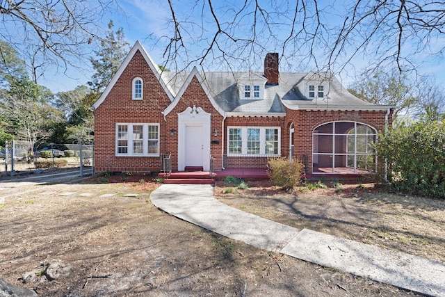 view of front facade with a sunroom, brick siding, and a chimney