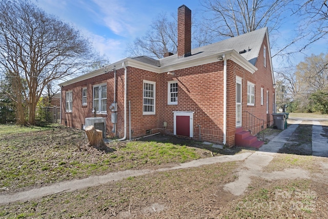 view of home's exterior featuring driveway, entry steps, a chimney, and brick siding