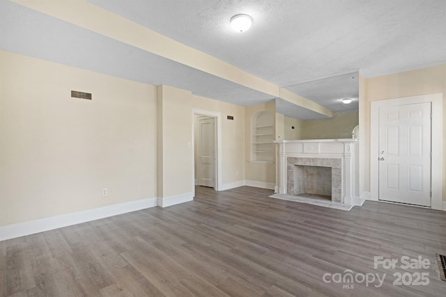 unfurnished living room featuring a fireplace, baseboards, a textured ceiling, and wood finished floors