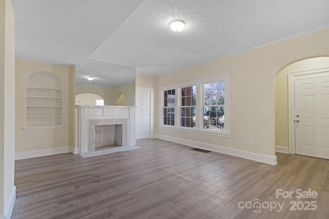 unfurnished living room with baseboards, a tiled fireplace, wood finished floors, a textured ceiling, and built in shelves