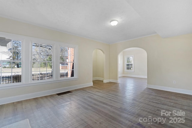 spare room featuring baseboards, visible vents, arched walkways, wood finished floors, and a textured ceiling