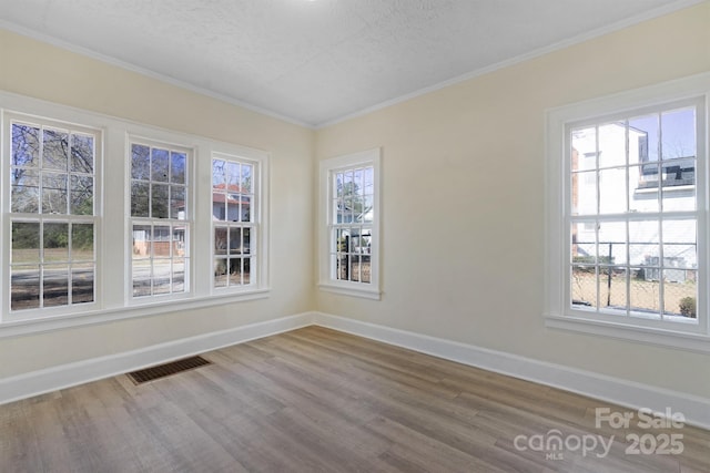 spare room with ornamental molding, visible vents, baseboards, and wood finished floors