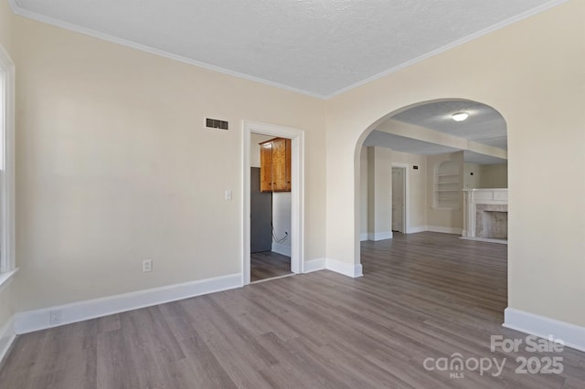 spare room with a textured ceiling, crown molding, wood finished floors, and baseboards