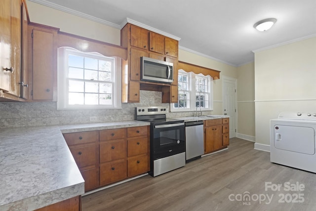 kitchen featuring brown cabinets, washer / clothes dryer, light countertops, appliances with stainless steel finishes, and wood finished floors