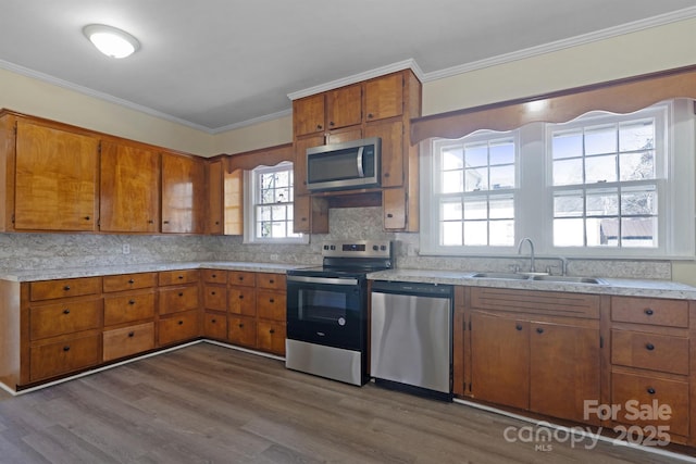 kitchen featuring brown cabinets, ornamental molding, stainless steel appliances, and a sink