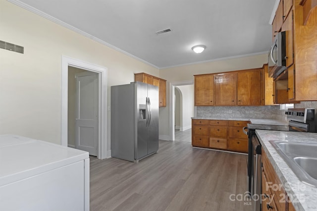 kitchen with appliances with stainless steel finishes, brown cabinets, visible vents, and tasteful backsplash