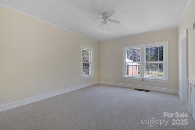 empty room with crown molding, visible vents, light carpet, ceiling fan, and baseboards