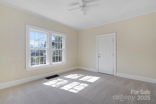 carpeted spare room with a ceiling fan, visible vents, crown molding, and baseboards