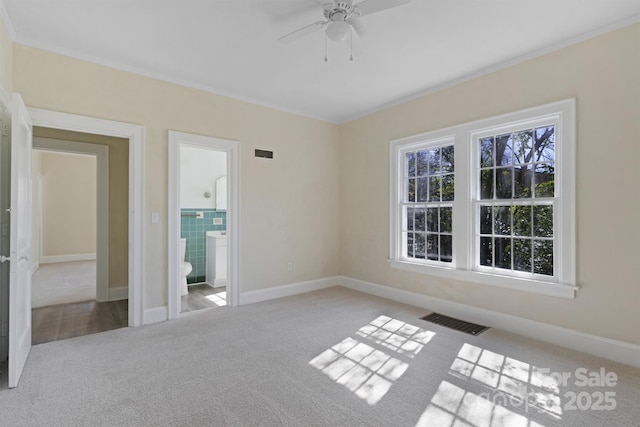 empty room featuring carpet floors, visible vents, crown molding, and baseboards