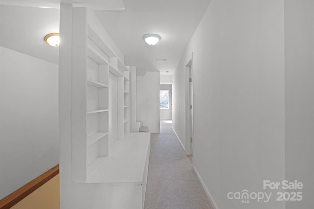 hall featuring baseboards, built in features, and light colored carpet