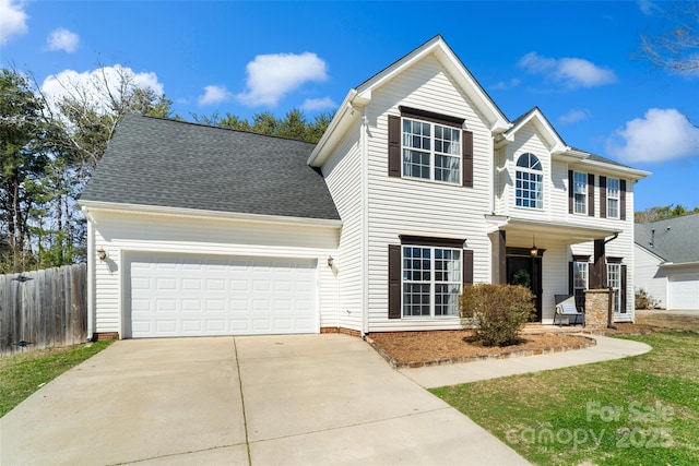 traditional home featuring driveway, an attached garage, fence, and a shingled roof