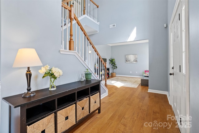 foyer entrance featuring baseboards, visible vents, stairway, wood finished floors, and a high ceiling