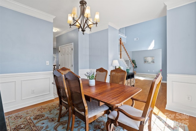 dining area featuring light wood-style floors, ornamental molding, stairway, wainscoting, and an inviting chandelier