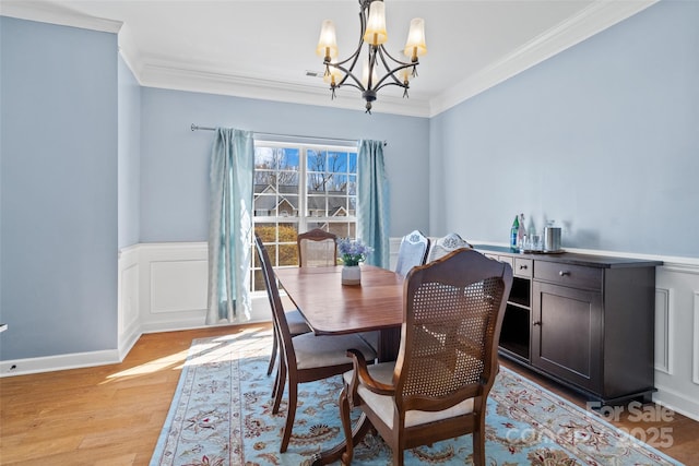 dining space featuring a wainscoted wall, ornamental molding, a chandelier, and light wood-style floors