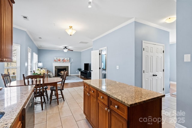 kitchen with light tile patterned floors, a ceiling fan, a lit fireplace, a center island, and brown cabinetry