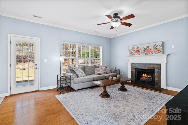 living room featuring ceiling fan, light wood-style flooring, a fireplace with flush hearth, baseboards, and ornamental molding