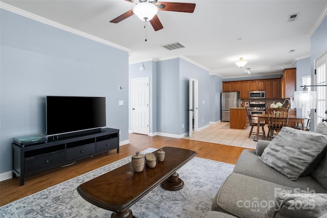 living room featuring light wood-style floors, baseboards, visible vents, and ornamental molding