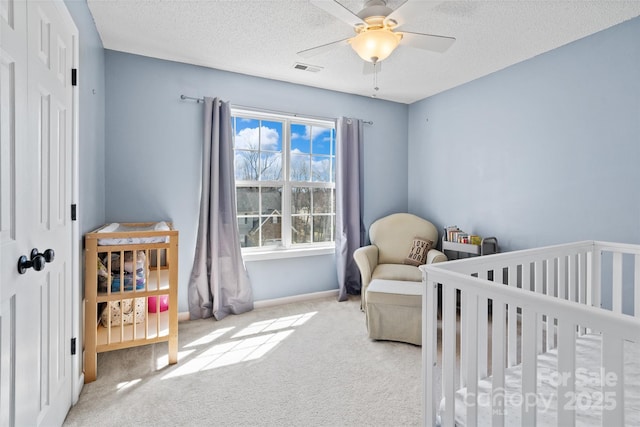 bedroom featuring a nursery area, a textured ceiling, carpet, and visible vents