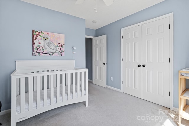 carpeted bedroom with a ceiling fan, a closet, a crib, and baseboards