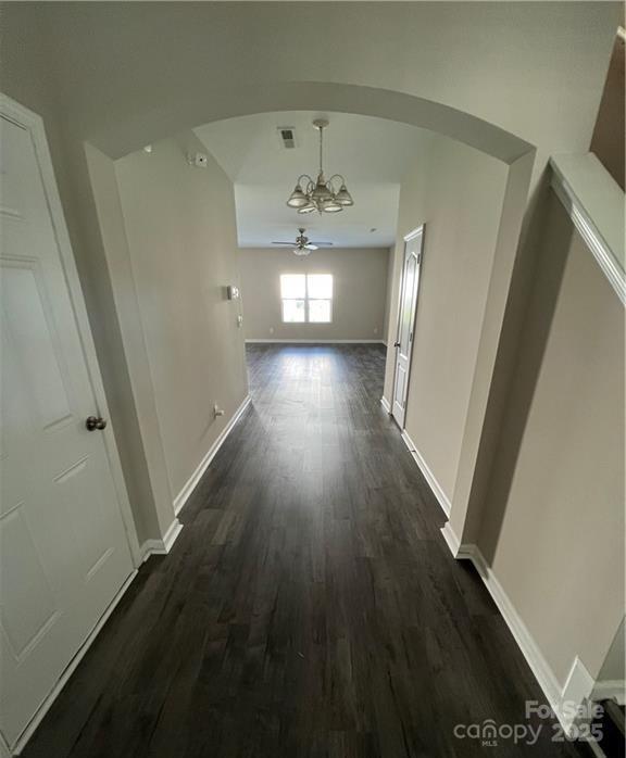 hallway featuring dark wood-style floors, visible vents, arched walkways, and baseboards