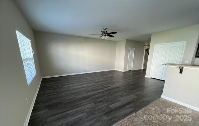 spare room with dark wood-style flooring, a ceiling fan, and baseboards