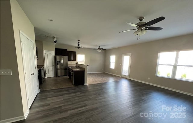 kitchen with a sink, baseboards, open floor plan, dark wood-style floors, and stainless steel fridge