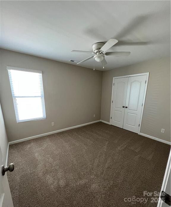 unfurnished bedroom with baseboards, dark carpet, and a closet