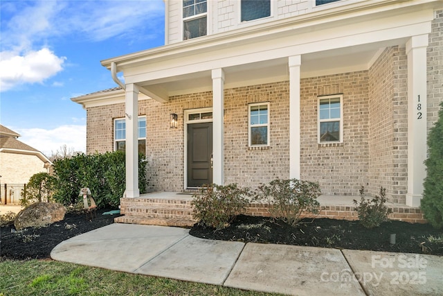 doorway to property featuring a porch and brick siding