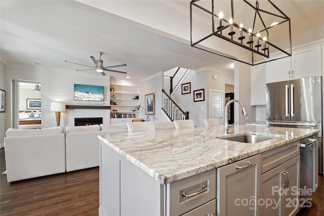 kitchen featuring an island with sink, ceiling fan, freestanding refrigerator, a lit fireplace, and a sink