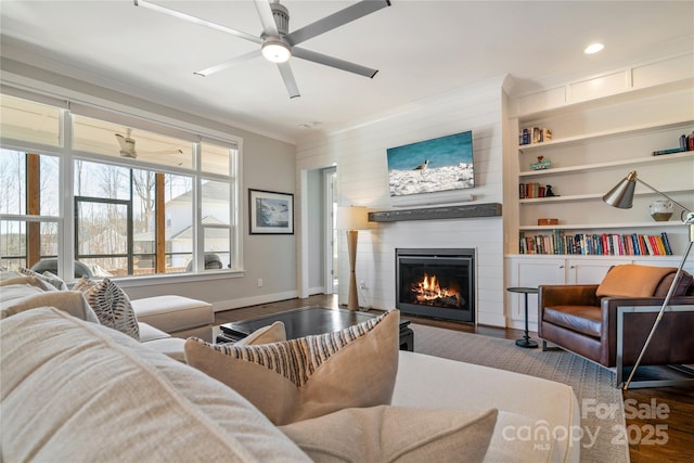 living room featuring built in shelves, a large fireplace, ceiling fan, wood finished floors, and baseboards