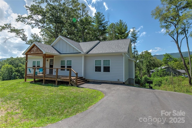 view of front of home with driveway, a shingled roof, a deck, board and batten siding, and a front yard