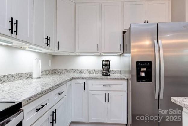 kitchen with light stone countertops, white cabinetry, and stainless steel refrigerator with ice dispenser