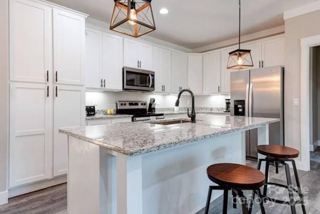 kitchen with white cabinets, dark wood-style floors, a breakfast bar area, stainless steel appliances, and a sink