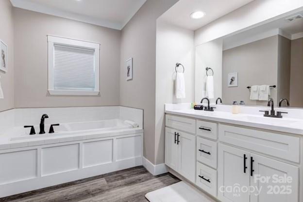 bathroom with wood finished floors, visible vents, a sink, a bath, and double vanity