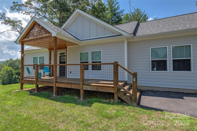 rear view of property with board and batten siding, roof with shingles, a lawn, and a wooden deck