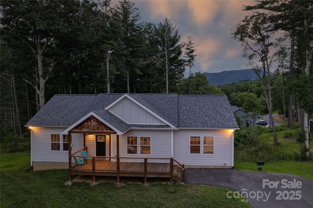 view of front of home with a deck with mountain view, aphalt driveway, roof with shingles, a lawn, and board and batten siding