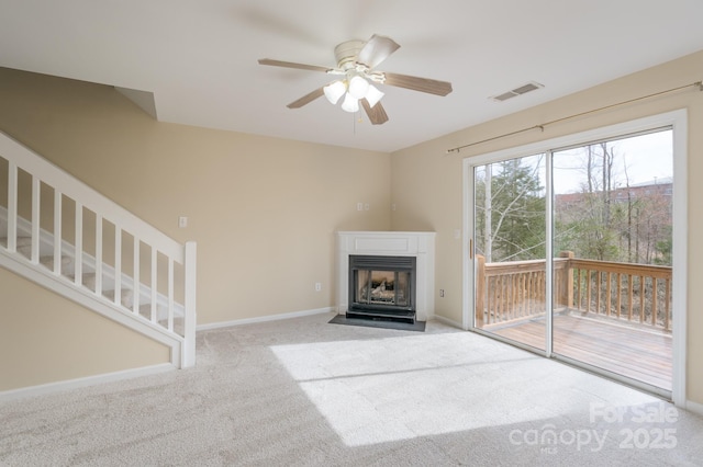 unfurnished living room featuring baseboards, visible vents, a fireplace with flush hearth, stairs, and carpet flooring