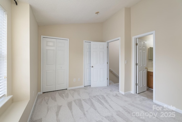 unfurnished bedroom with multiple closets, lofted ceiling, light carpet, and baseboards