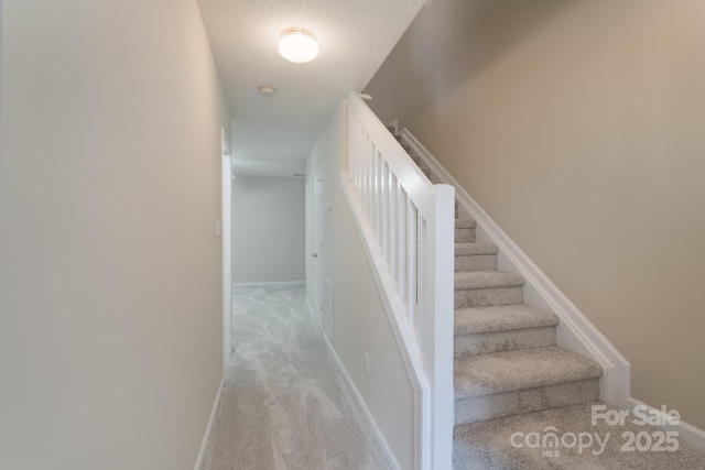 staircase featuring carpet, a textured ceiling, and baseboards