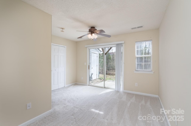 carpeted empty room with a ceiling fan, visible vents, a textured ceiling, and baseboards